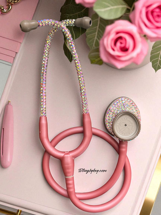 Pink stethoscope with rhinestone accents on a surface with flowers and a pen.
